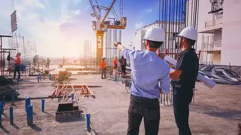 Two construction workers on a site looking at plans, representing finding a subcontractor.